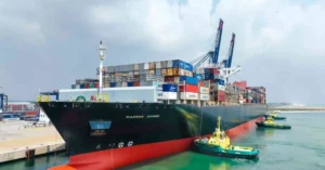 A ship loaded with colorful containers leaving Lagos Port with the skyline in the background.