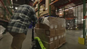 Warehouse scene showing stacked pallets, forklifts, and staff preparing packages for dispatch.